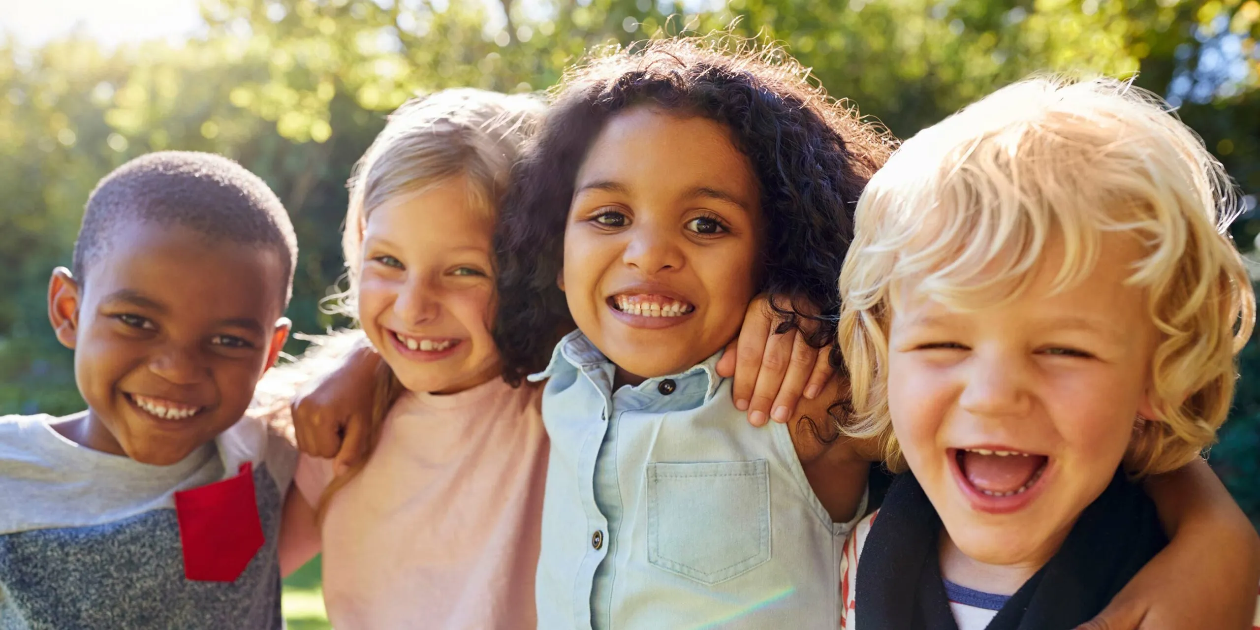 Four smiling children with their arms around each other outdoors